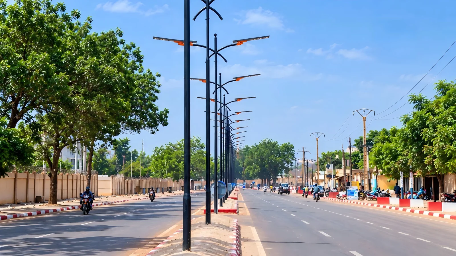 A row of double-arm all-in-one solar street lights along a tree-lined boulevard in West Africa by day