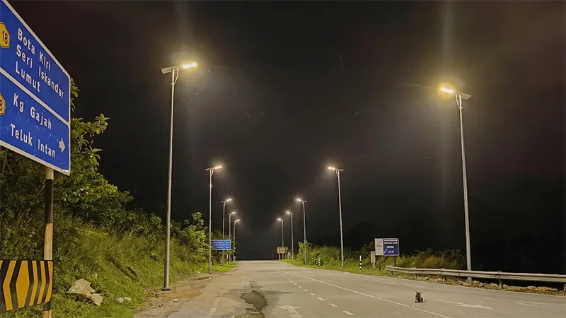 A nighttime view of a dirt field illuminated by three tall streetlights against a dark sky.