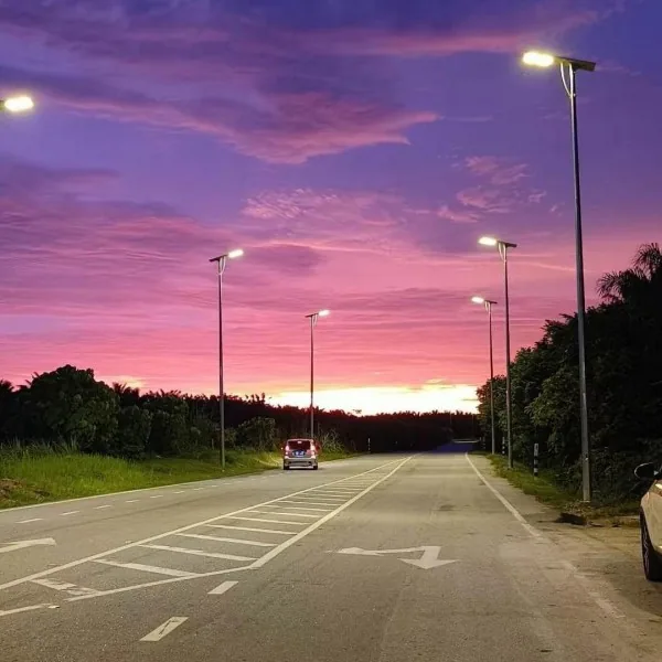 A wide road with solar-powered street lights on both sides under a dramatic purple and pink sunset sky.
